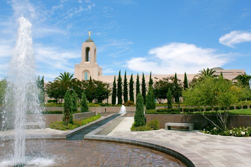 The water from a fountain on the grounds of the Newport Beach California Temple, with the temple and temple’s trees seen behind it.