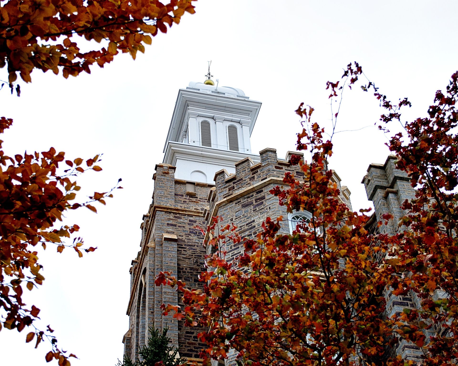 The Logan Utah Temple in the fall, including the spire, exterior of the temple, and scenery.