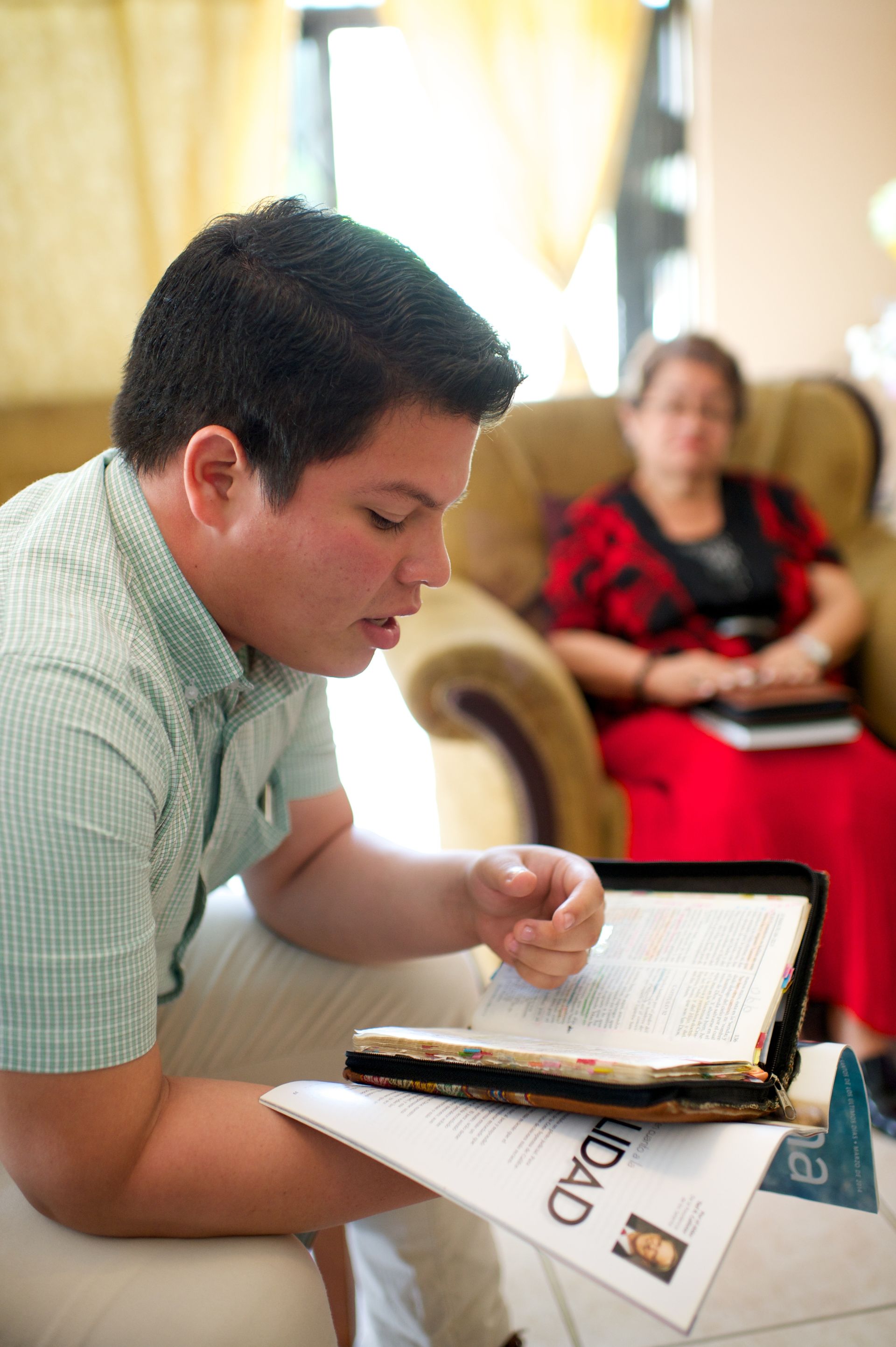 A young man from Ecuador reading the scriptures and a Liahona magazine.