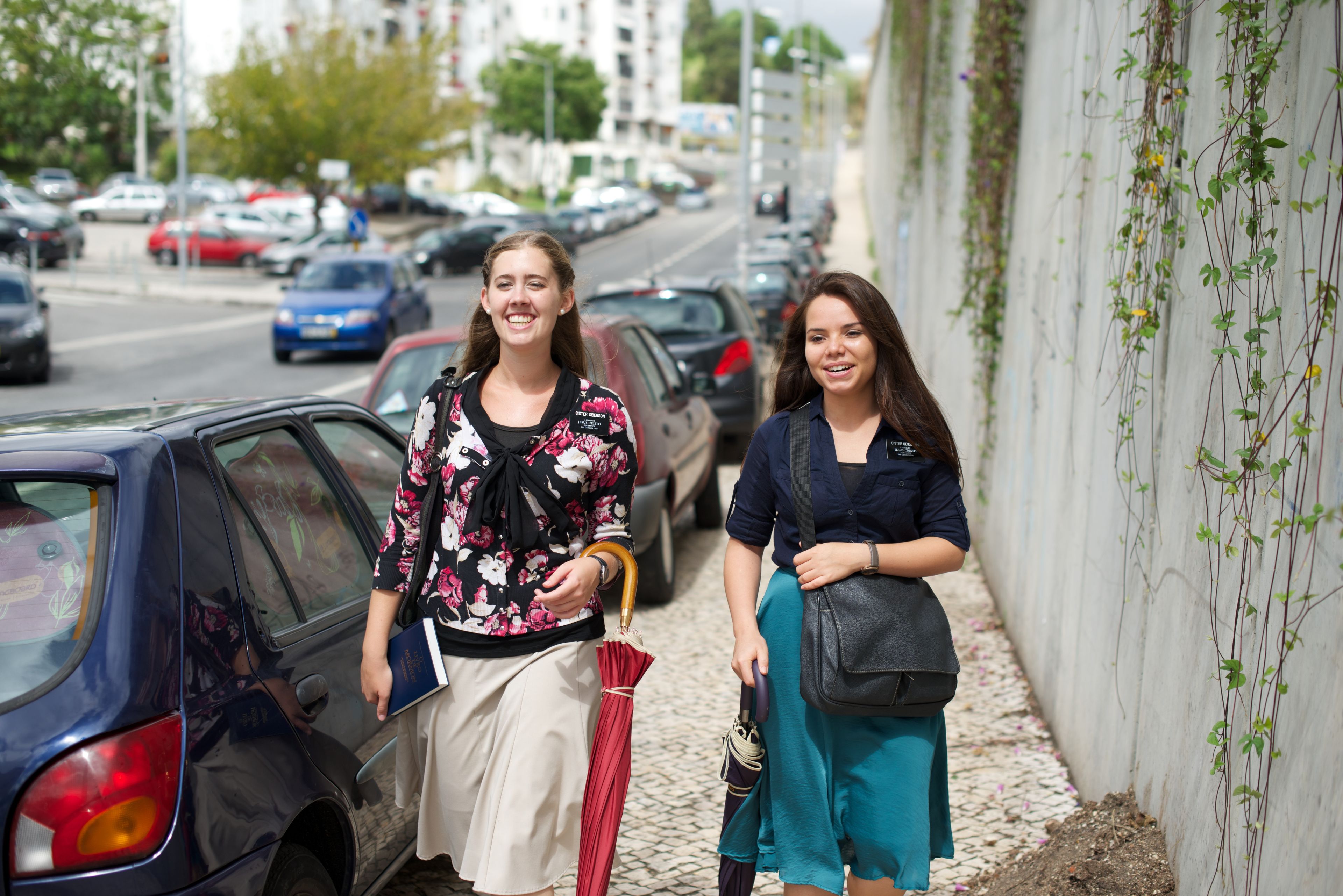Sister missionaries walking down a street and holding umbrellas.