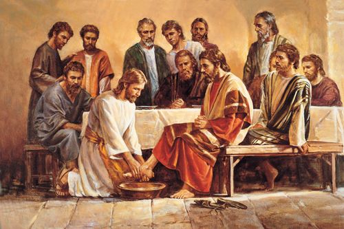 Christ in white robes with a yellow sash, kneeling to wash the feet of one of His Apostles while the other eleven sit around the table.