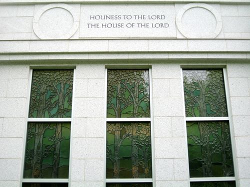 Three stained-glass windows portraying the Sacred Grove on the Palmyra New York Temple, with “Holiness to the Lord: The House of the Lord” over them.