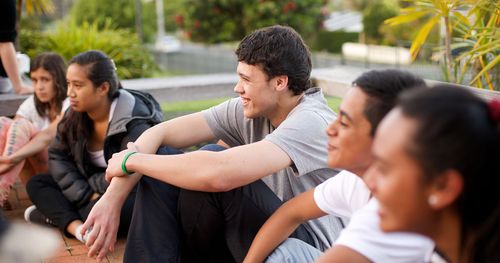 Youth engaged in a group activity. They are seated in a circle in an outdoor setting.