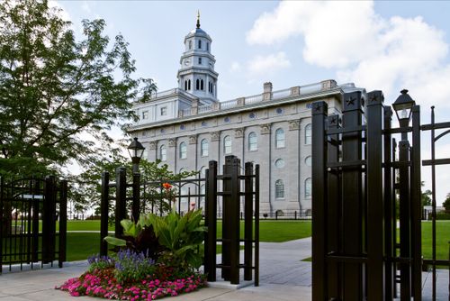 A side view of the Nauvoo Illinois Temple, seen through the rungs and gates of a black fence that surrounds the temple grounds.