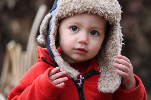 A toddler boy wearing a winter hat and a red fleece jacket.
