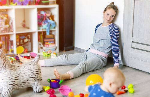 mother sitting on floor, while a child plays with toys