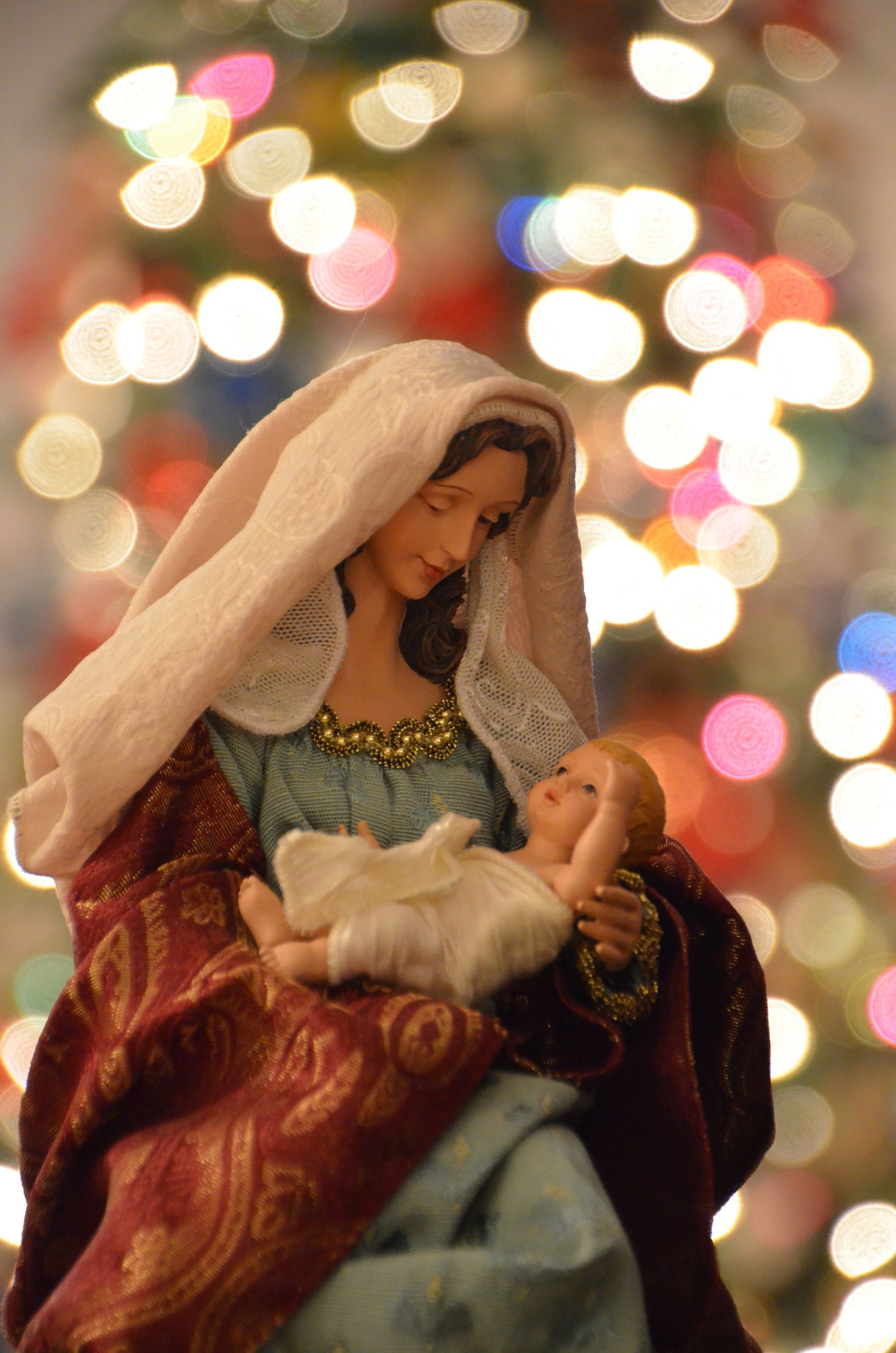 A Nativity figurine representing Mary and Jesus in front of colorful Christmas lights.