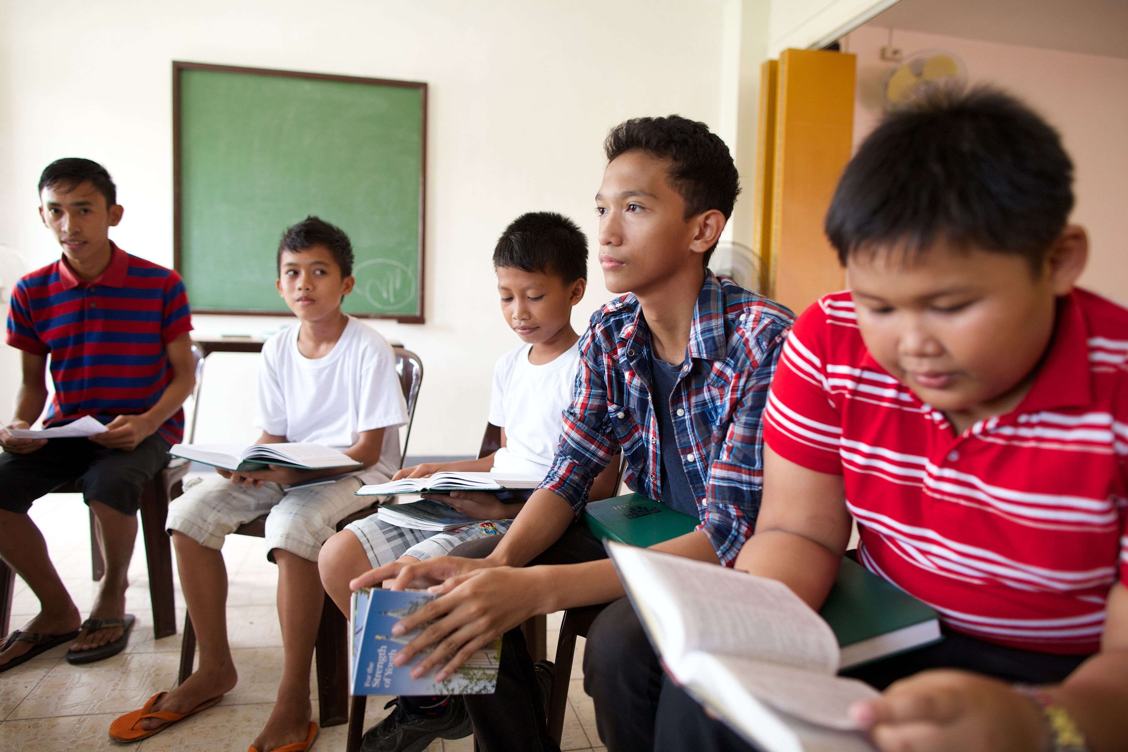 A group of young men from the Philippines sitting in a classroom at church and reading Church materials.