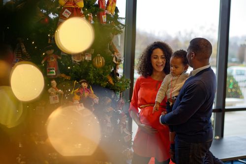 A father, mother, and young son smiling while standing next to a decorated Christmas tree.