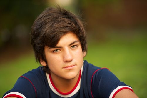 A portrait of a young man in a sports jersey sitting outside and looking straight ahead.