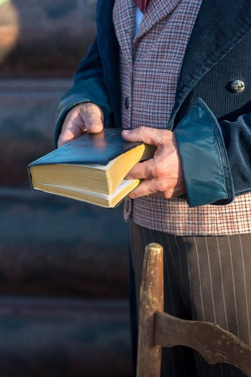 A close-up view of an actor from the Martin Harris Pageant standing and holding closed scriptures with his finger in the middle of the pages.
