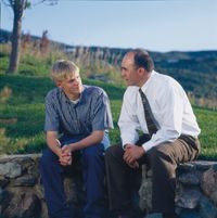 A father sitting on a stone fence with his teenage son. The father and son are looking at each other as they counsel together. Posed by models.