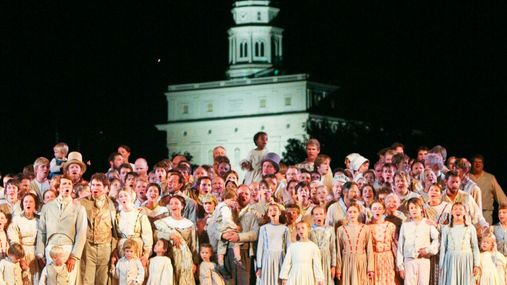 A large group of performers dressed in pioneer era clothing standing on a stage.