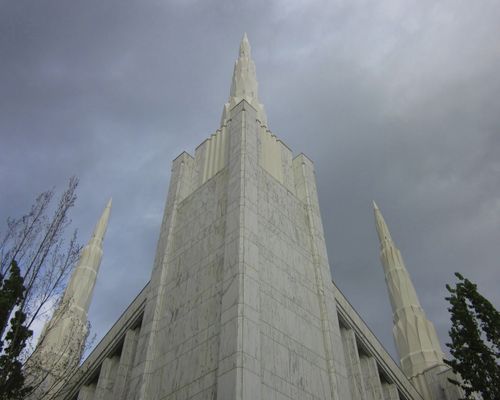Three spires at the front of the Portland Oregon Temple seen from the ground, looking up toward a pale gray sky.
