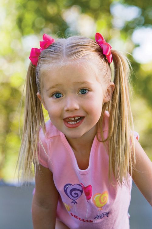 A little girl with blonde hair in ponytails and pink bows, wearing a light pink shirt.