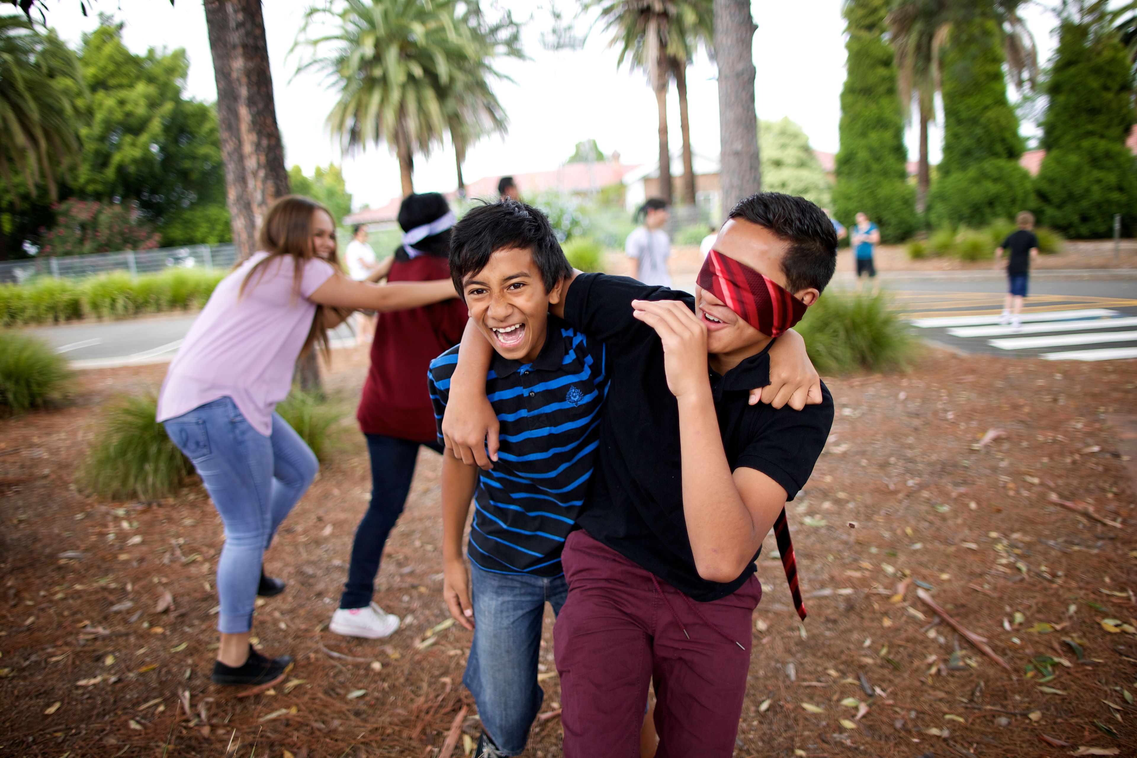 A group of young men and young women playing a leadership activity that includes blindfolding a partner and leading him or her outside.  