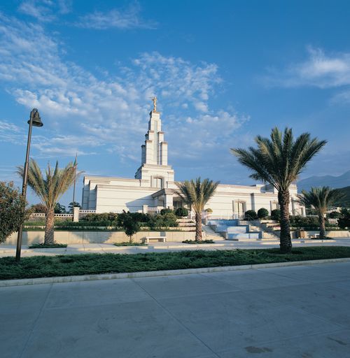 A view from afar of the Monterrey Mexico Temple, with its landscape of palm trees and other plants framing the entrance.