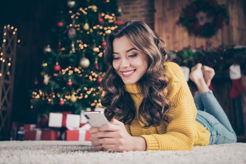 a woman holding a phone and lying down next to a Christmas tree