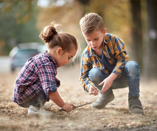 A brother and sister play with sticks and dead grass while playing outside.