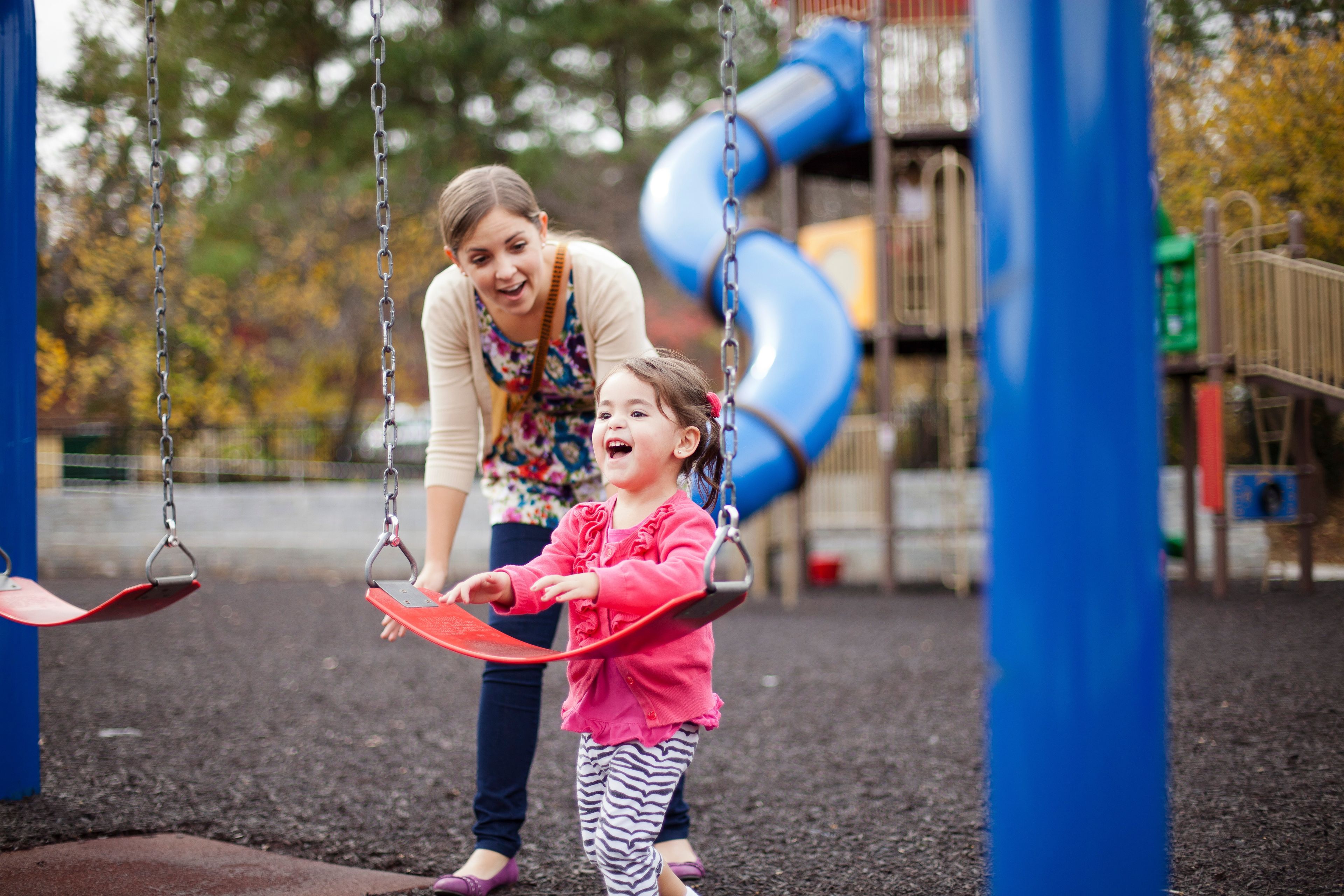 A mother helps her daughter onto a swing at a playground.