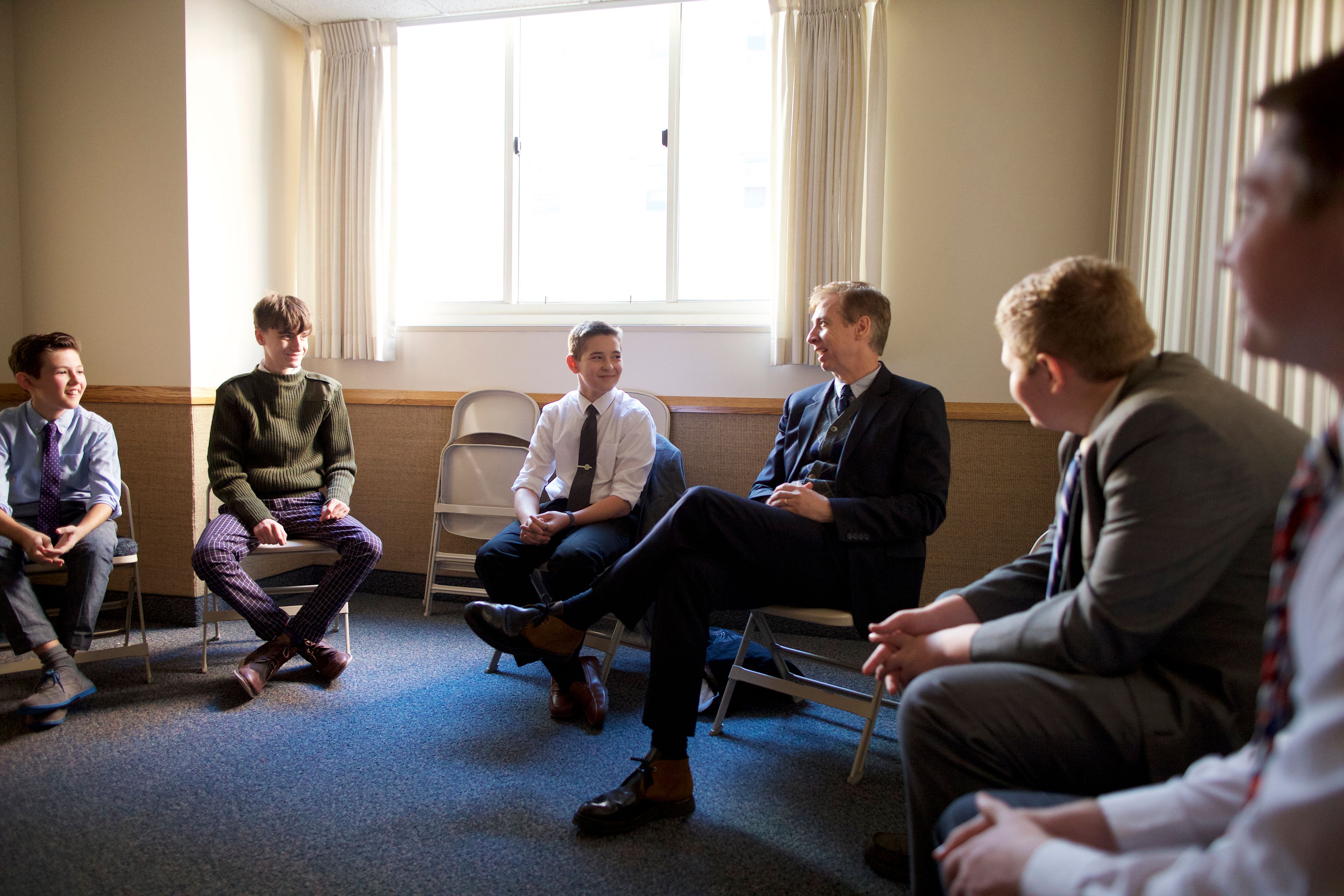 A quorum of young men in New York sit in a classroom and talk together.