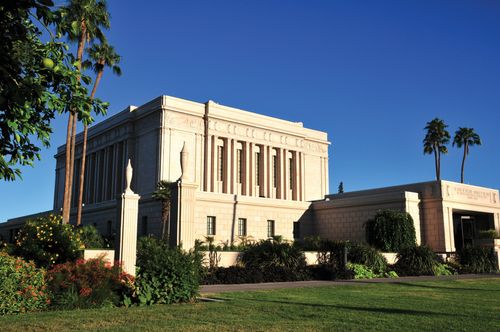The entrance of the Mesa Arizona Temple is viewed from the side, with a surrounding landscape of plants and trees.