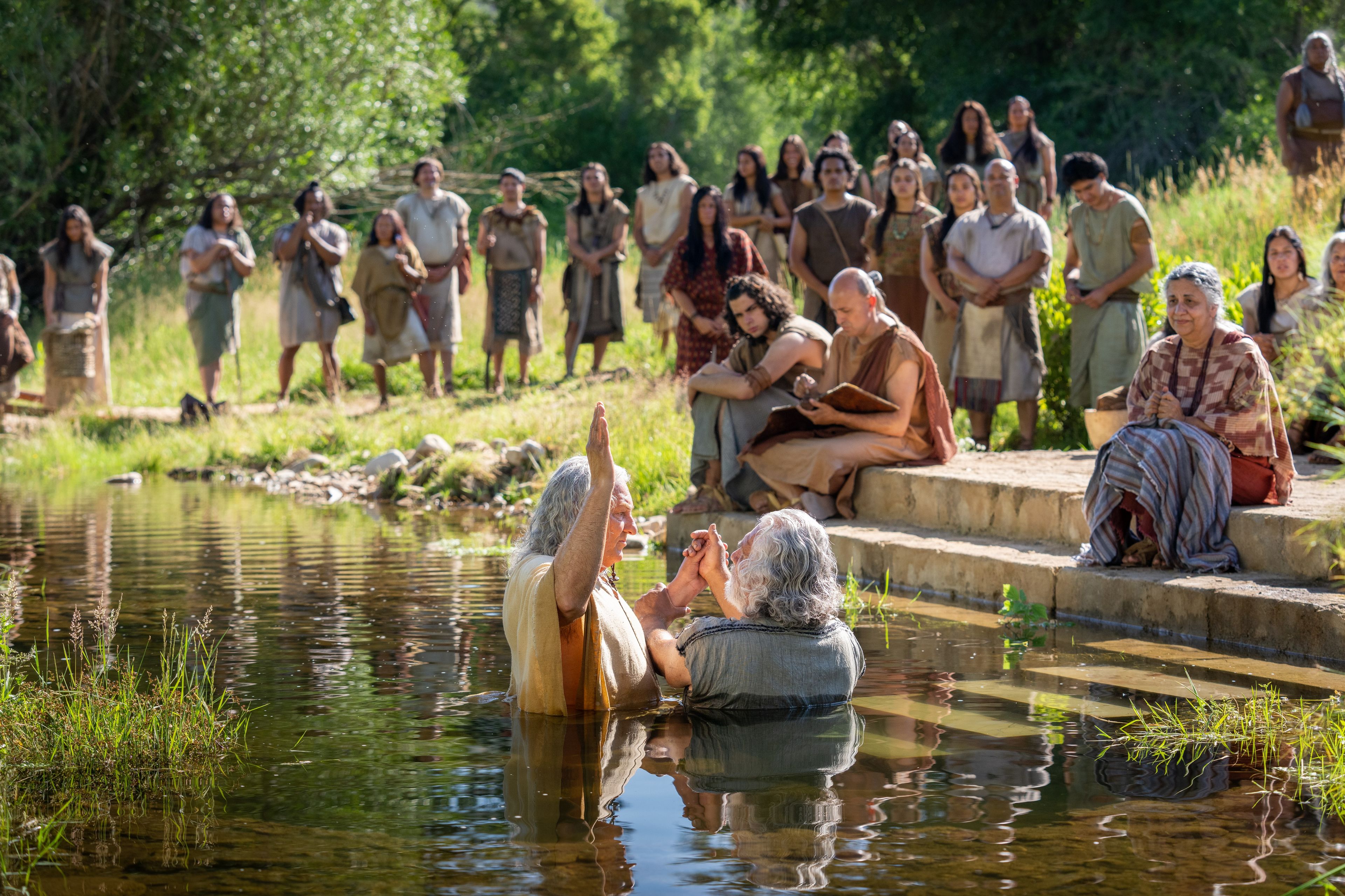 Nephi, son of Nephi, baptizes other Nephites in a river. Others (including Timothy) stand at the water's edge and watch.