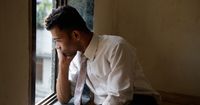 Young Adult Male Depression, Mumbai India.  Man looking out of a window and thinking.