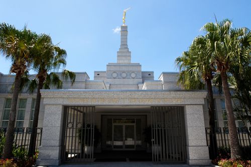The entrance to the Brisbane Australia Temple, with palm trees on either side and the spire overhead.