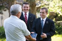 Elder missionaries giving an elderly man a Book of Mormon.