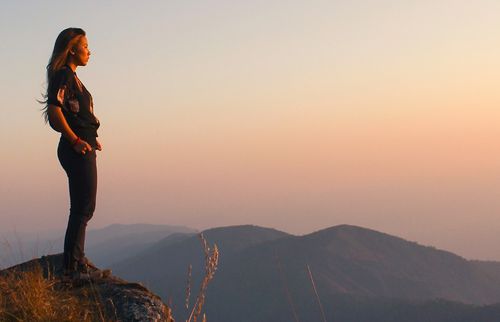 femme debout sur la crête d’une montagne regardant un coucher de soleil