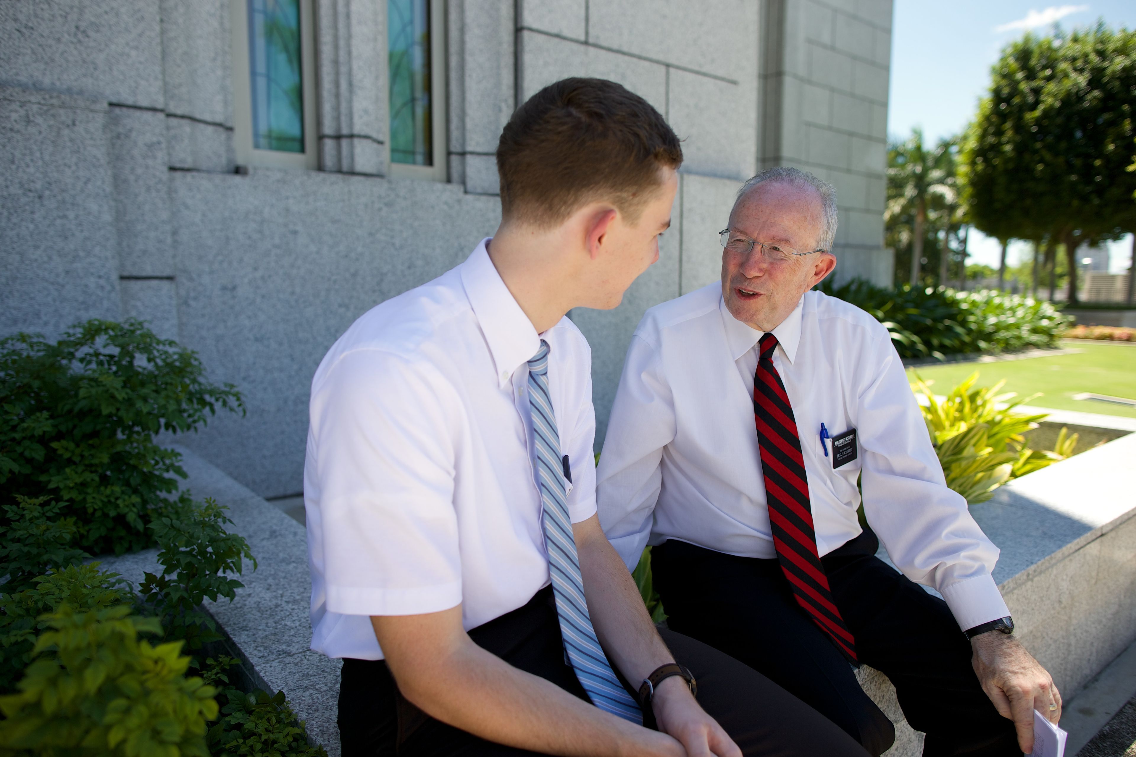 A senior elder missionary talking to an elder missionary outside a temple.