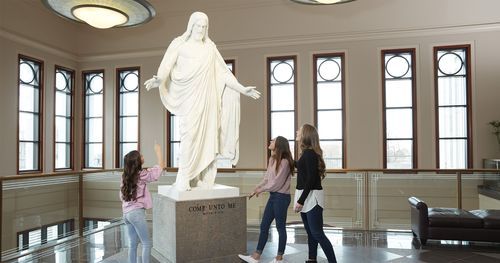 A family gathers inside the Conference Center. They are looking at a statue of the Christus.