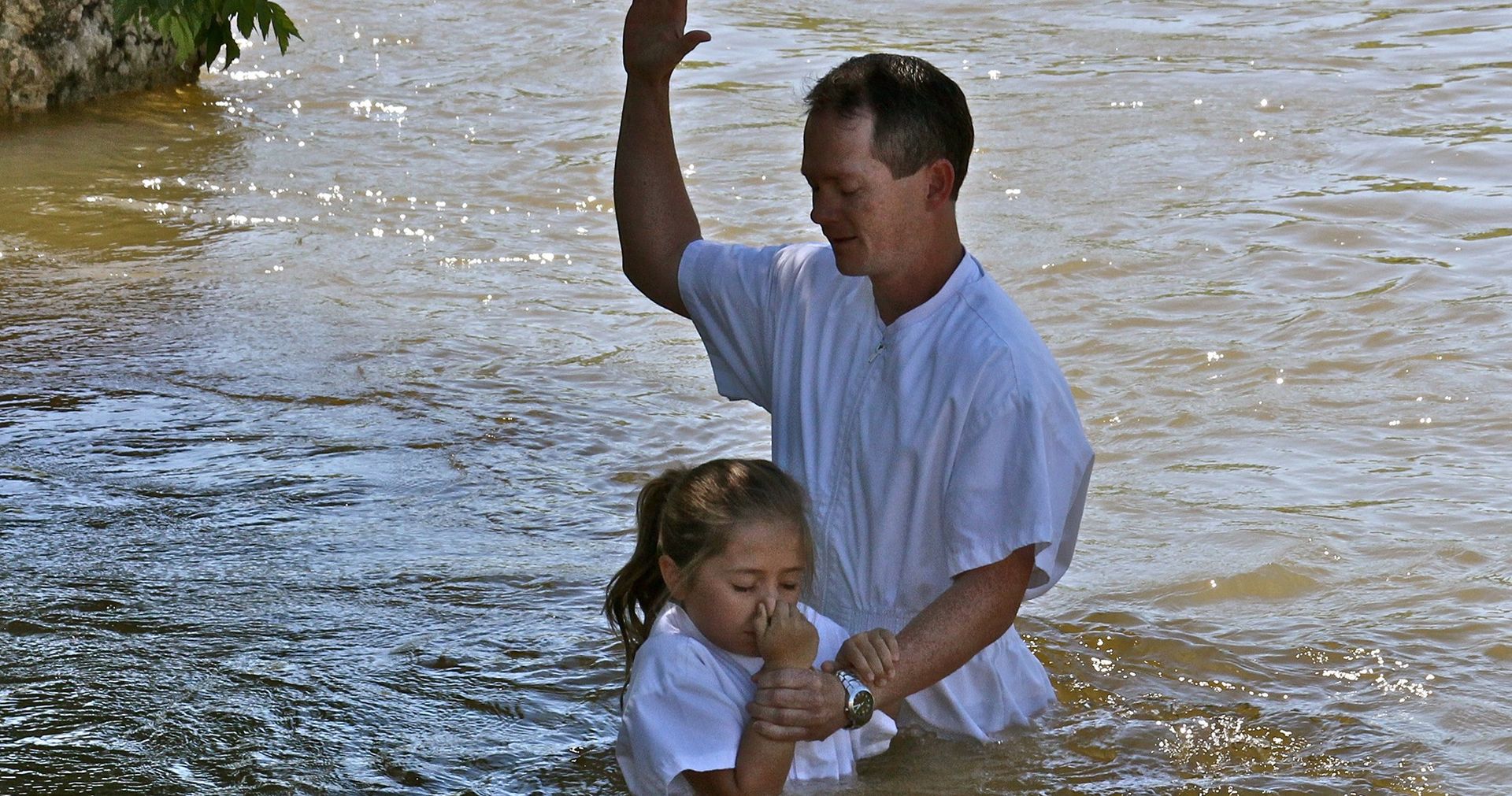 A man baptizing a little girl in a river.