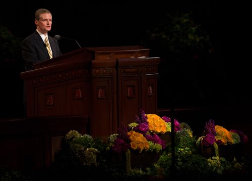 David A. Bednar in a yellow tie and black suit, standing at the pulpit to speak at general conference.