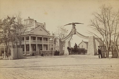 Black and white photo of the ornate Beehive house. Two people stand in the street in the foreground.