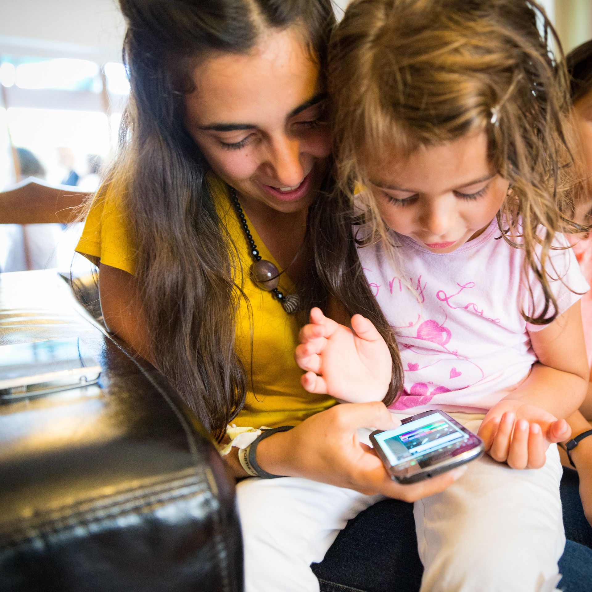 A little girl and her mother look at a smartphone together.  