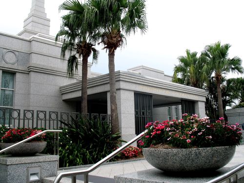 A large stone pot of flowers on the grounds of the Brisbane Australia Temple, with the temple’s entrance behind it.