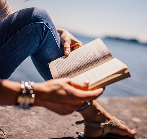 person reading book next to a lake