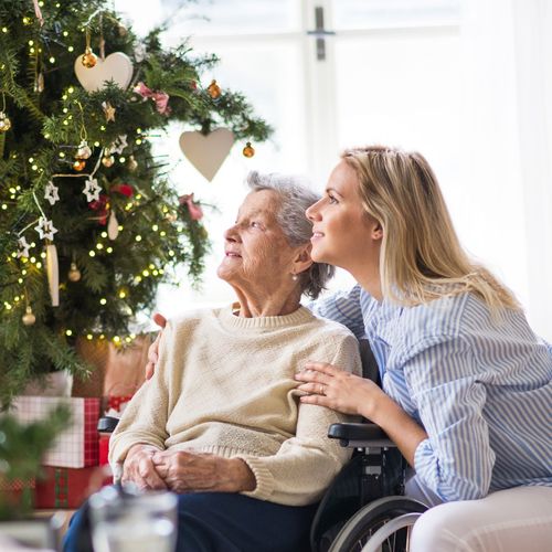 Una mujer más joven y una mujer mayor sentadas juntas al lado de un árbol de Navidad