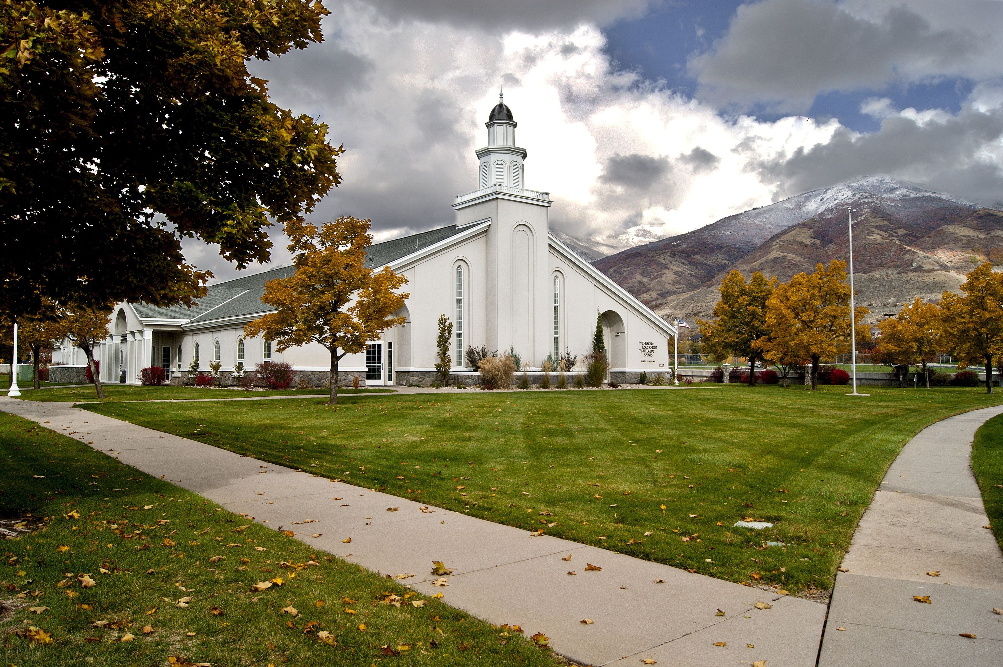 A white chapel with mountains and clouds in the background in Farmington, Utah.