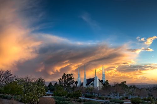 A distant view of the Las Vegas Nevada Temple at sunset, with orange light reflecting on the clouds overhead.