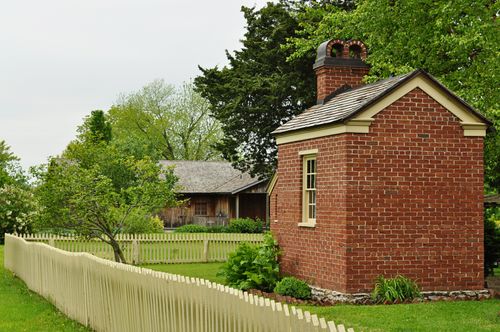 A small red-brick building sits on the lawn, surrounded by a white picket fence.