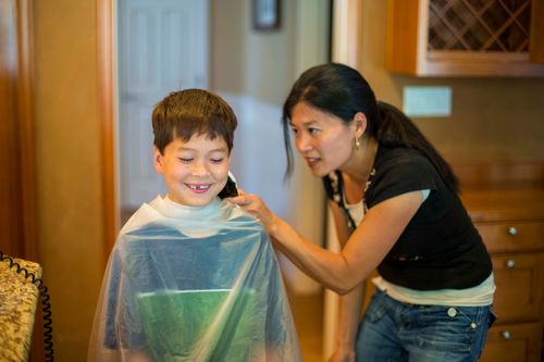 A mother cuts her son’s hair in their home.