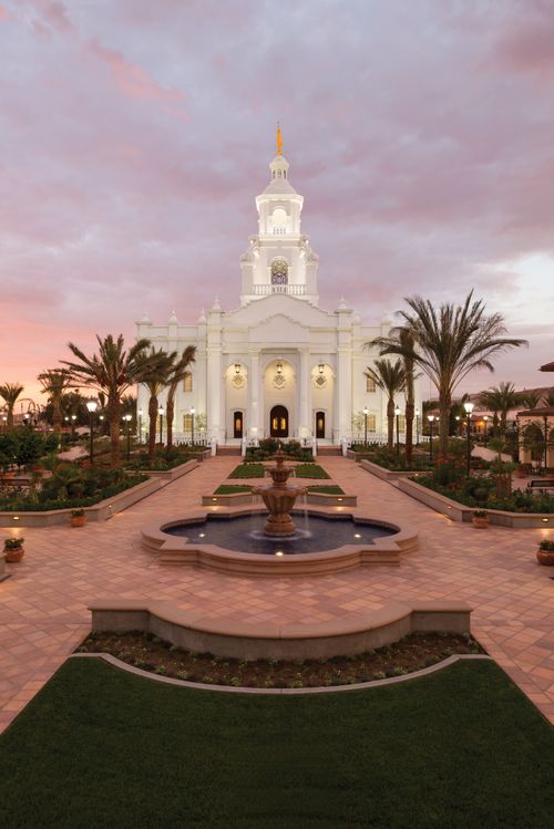 A fountain, sidewalks, and vegetation outside the Tijuana Mexico Temple, with a sunset in the background.