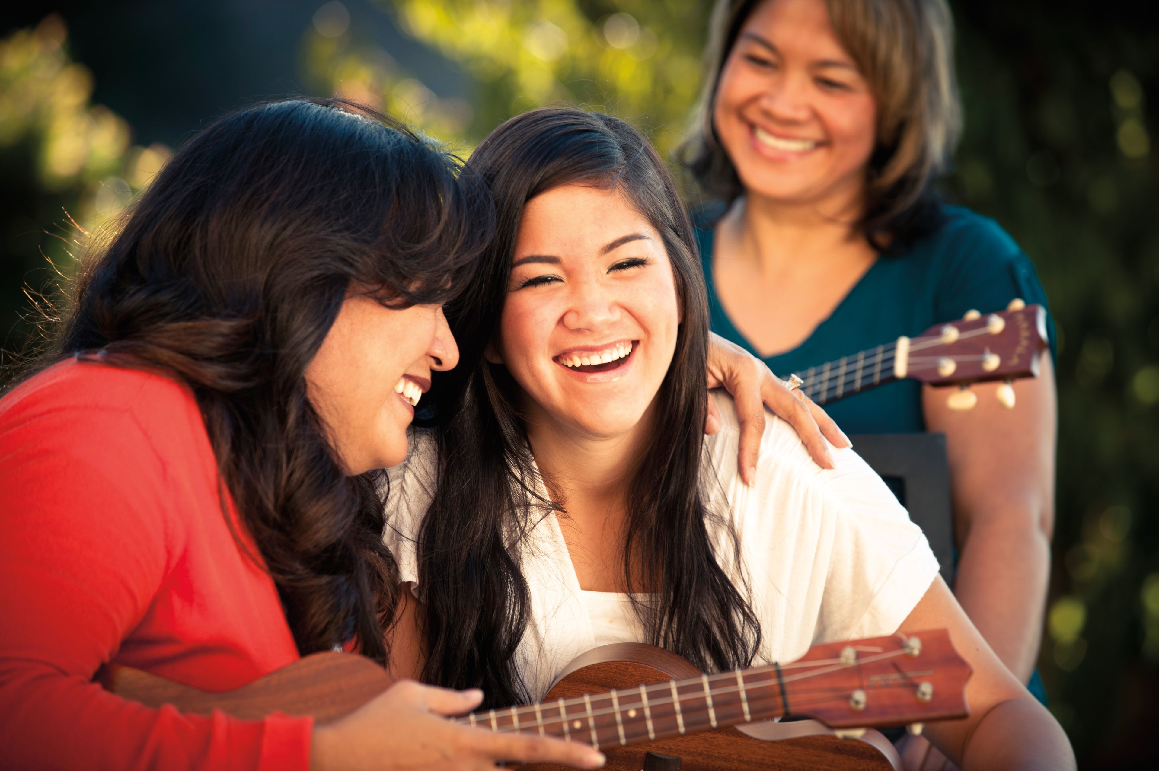 Three women sit together and play ukuleles.