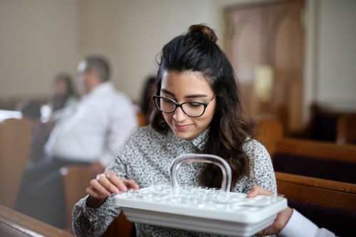 A young woman with dark hair and glasses takes the water from a sacrament tray.