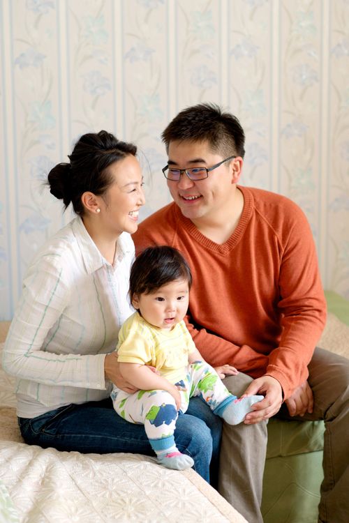 A mother and father sit on a bed with their baby daughter, and they all smile.