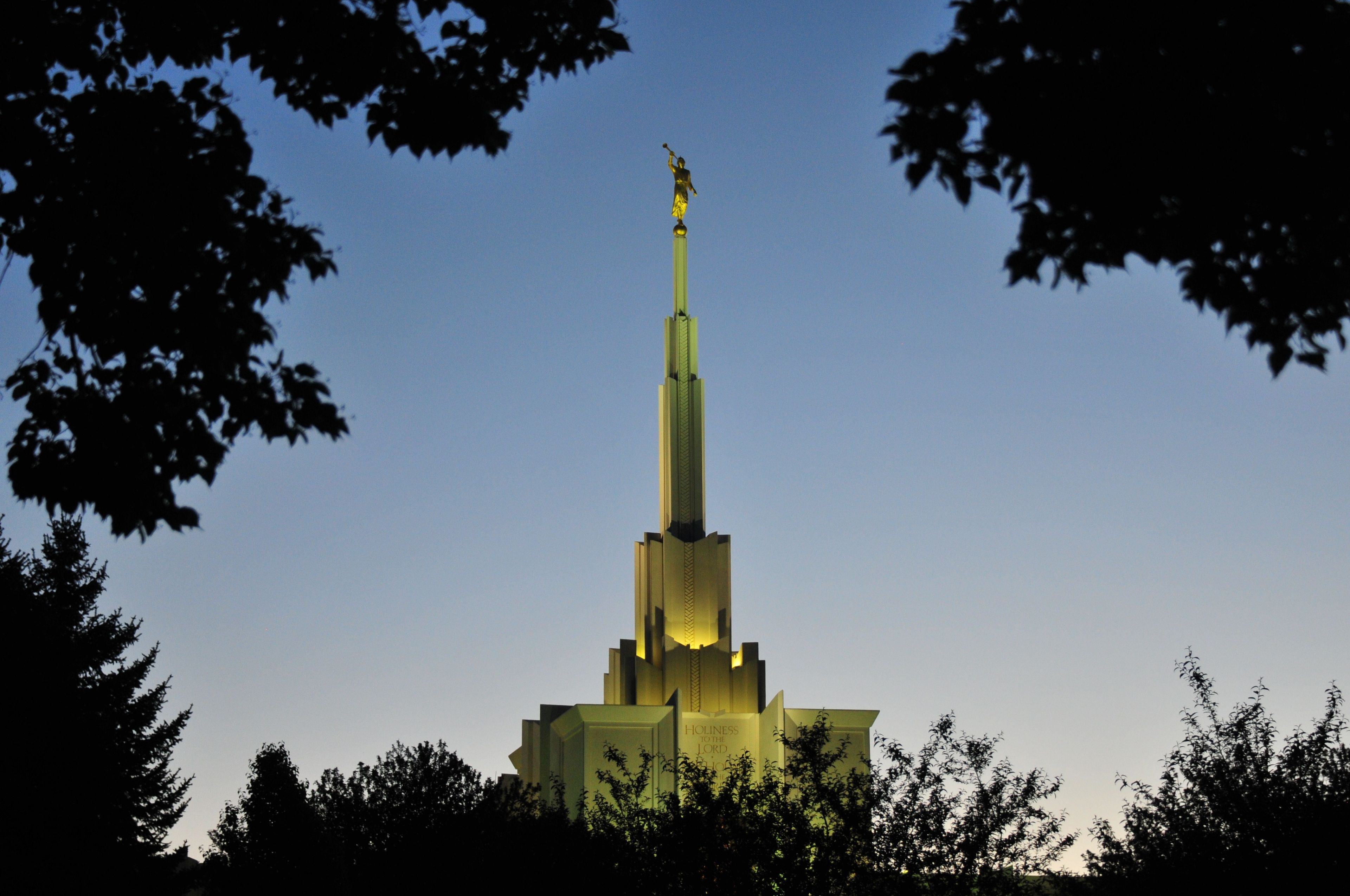 The spire of the Denver Colorado Temple is lit up at night.