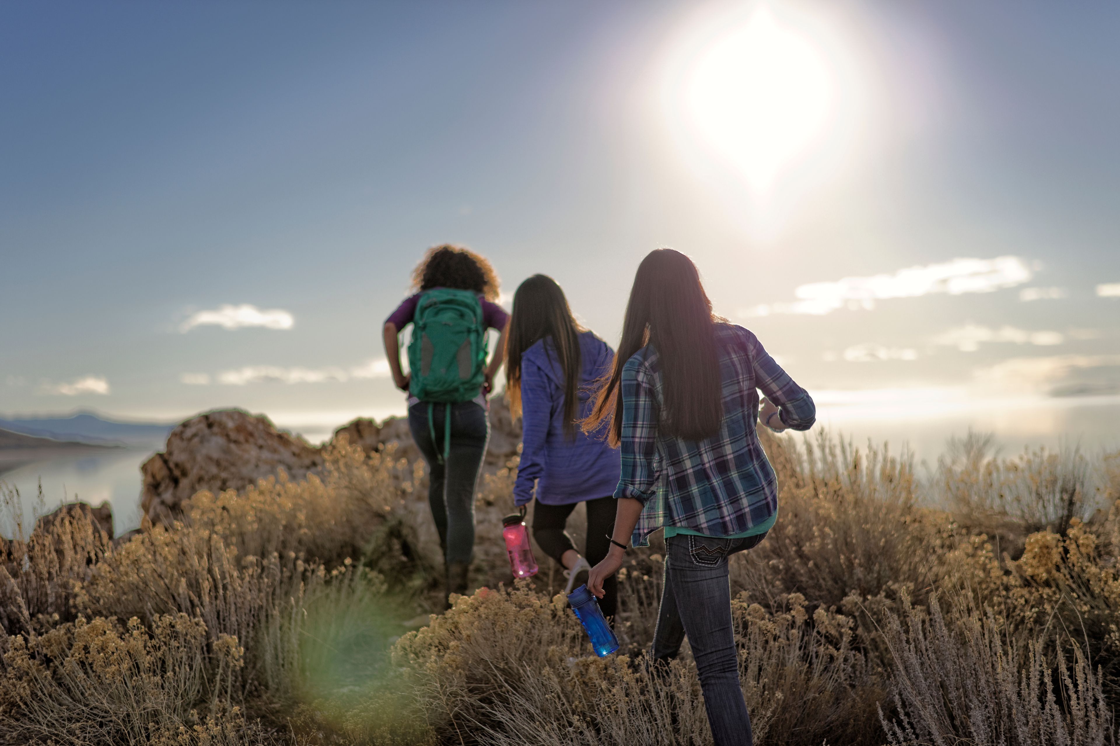 Three young women hike together over a hill during girls’ camp.  